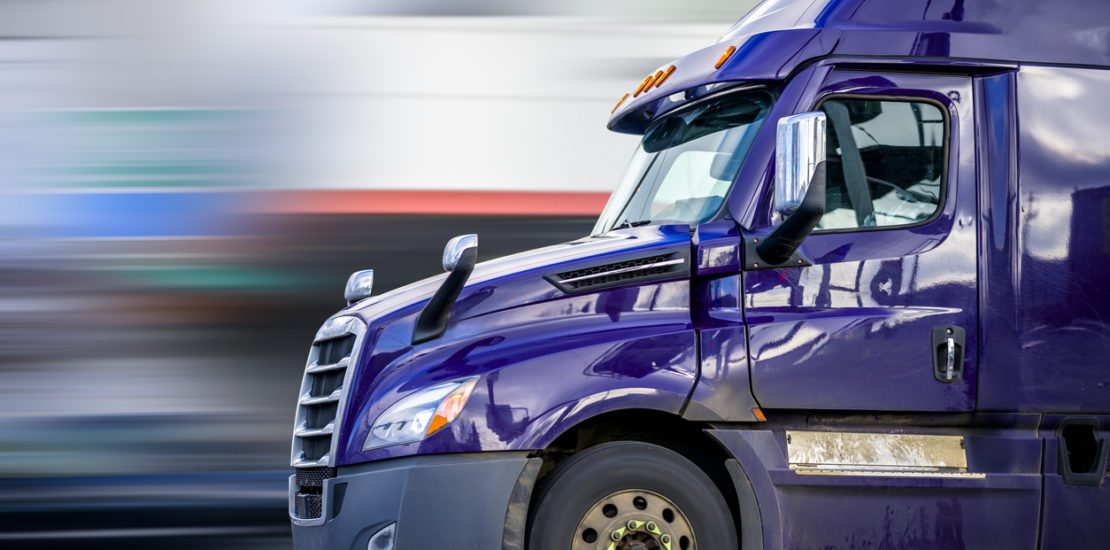 A purple semi truck in front of a blurred background.